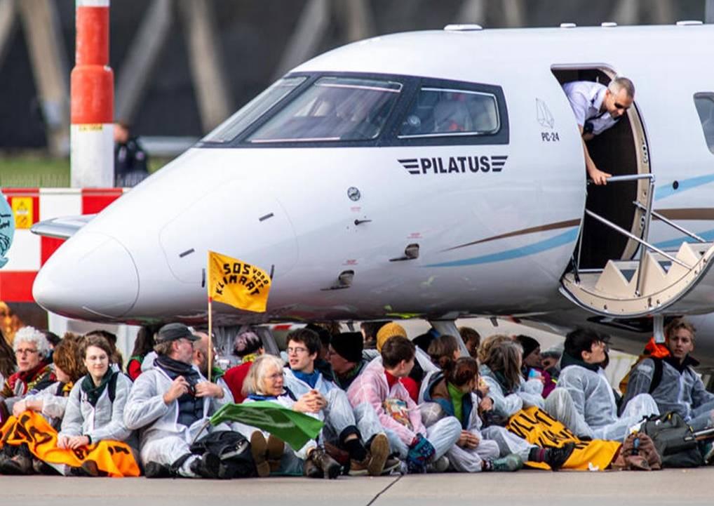 Activisten zitten voor een vliegtuig, om deze aan de grond te houden.