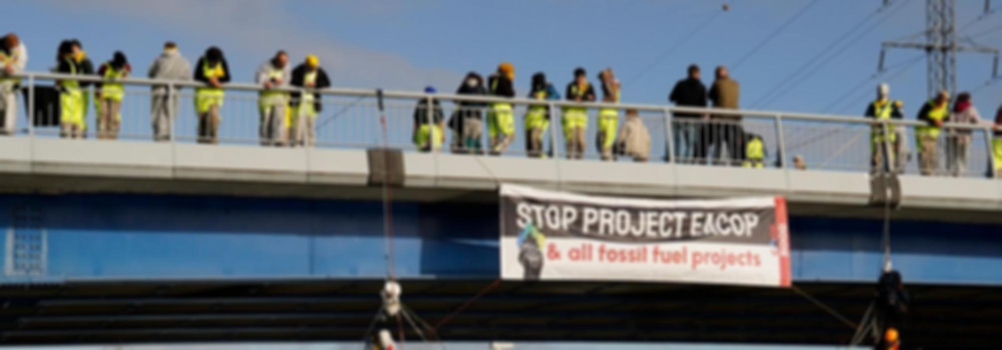 Activisten op een brug met spandoek 'stop project eacop & all fossil fuel projects'