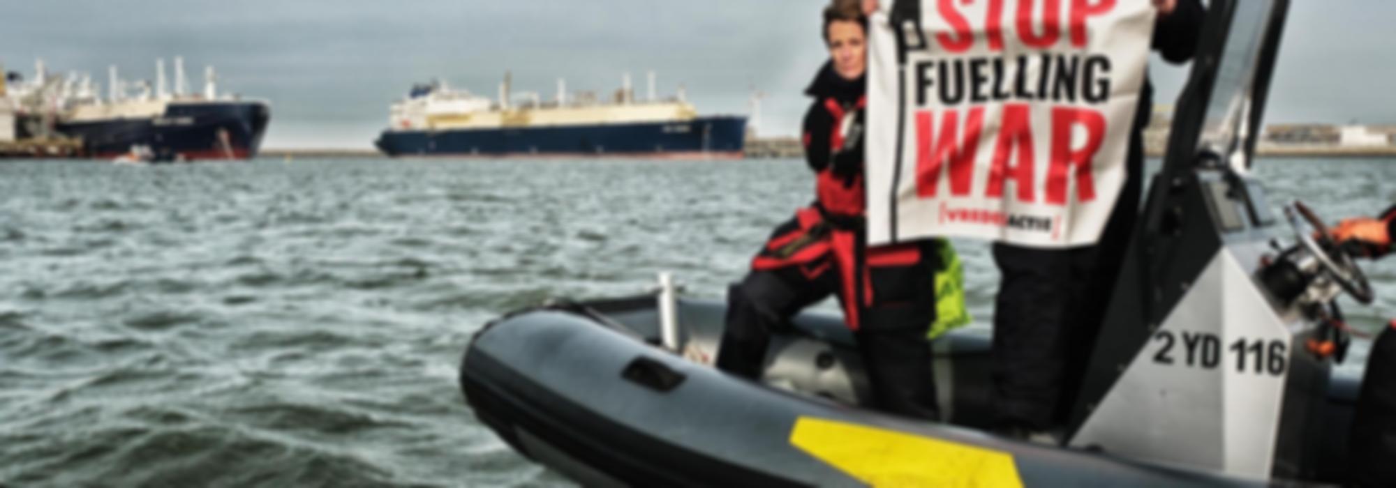 activist met banner stop fuelling war voor 2 gigantische LNG tankers in de haven van zeebrugge