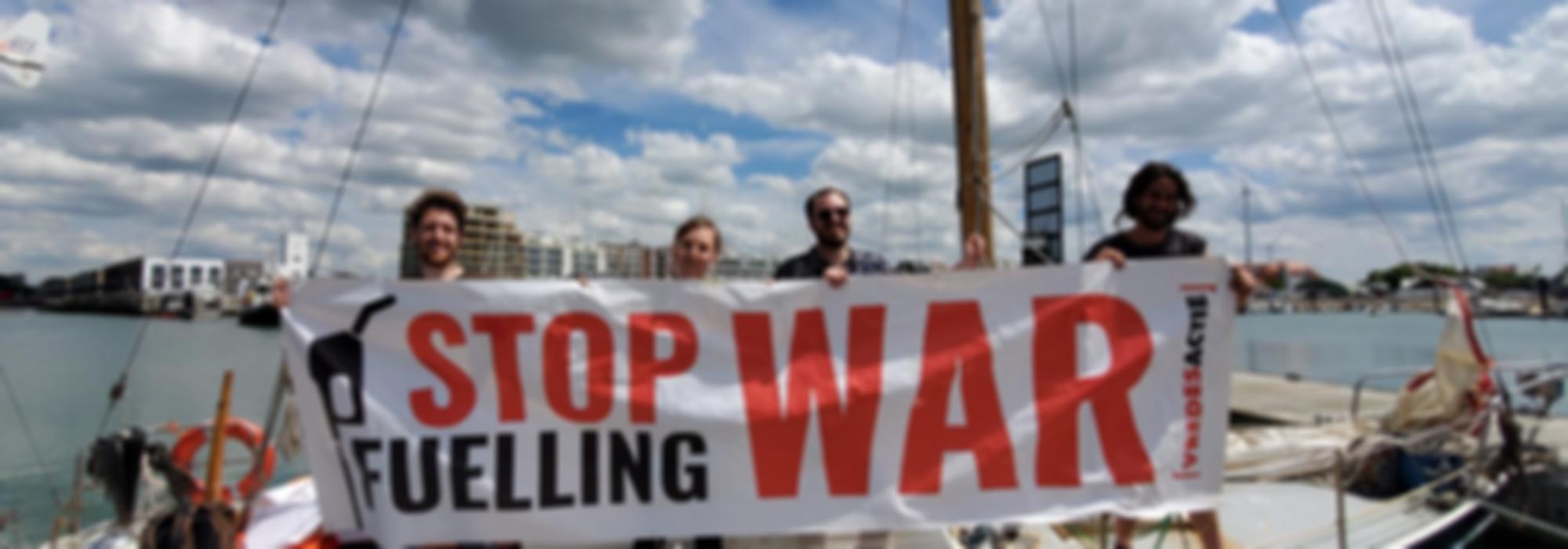 Vier mensen staan op een boot en houden een banner vast, waarop staat 'stop fuelling war'
