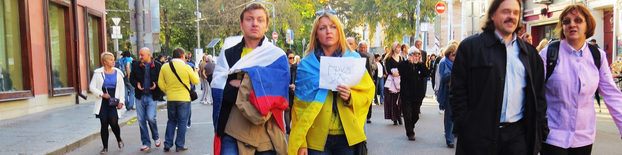 twee mensen op een vredesbetoging in Moskou. De ene is gedrapeerd in de Russische vlag, de andere in de Oekraiense.