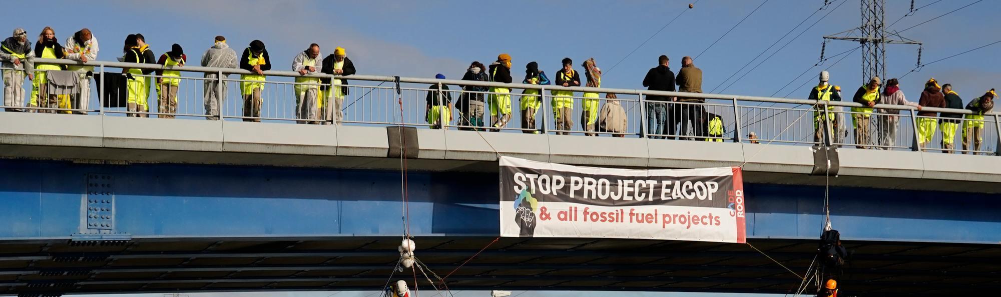 Mensen staan op een brug met een STOP EACOP banner