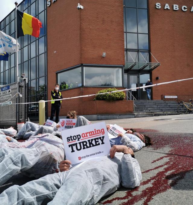 protest bij wapenfabrikant Sabca - mensen liggen op de grond in die-in. Iemand houdt bordje vast "Stop Arming Turkey"