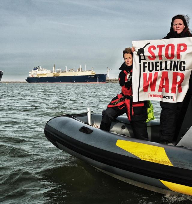 activist met banner stop fuelling war voor 2 gigantische LNG tankers in de haven van zeebrugge